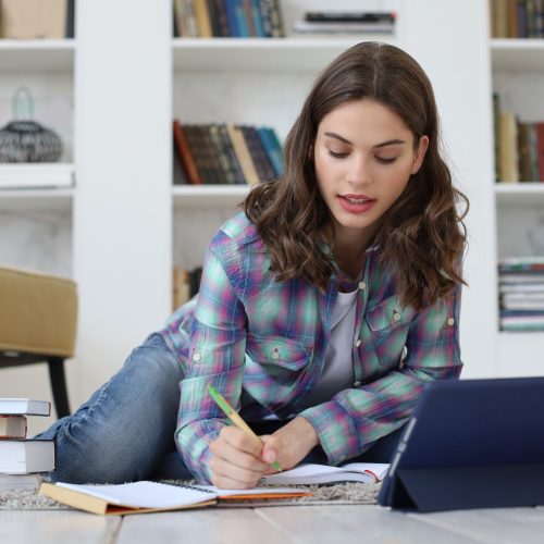 educacion-distancia-joven-estudiante-estudiando-casa-escribiendo-articulo-su-publicacion-sentada-piso-usando-tableta-contra-acogedor-interior-domestico-rodeada-pila-libros